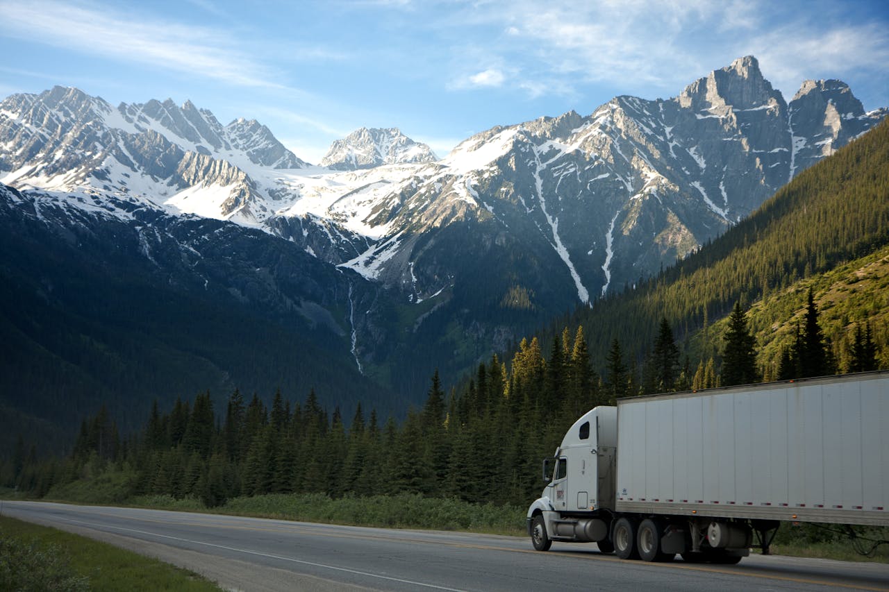 gallery-04 A semi-truck travels along a highway with snow-capped mountains in the background.